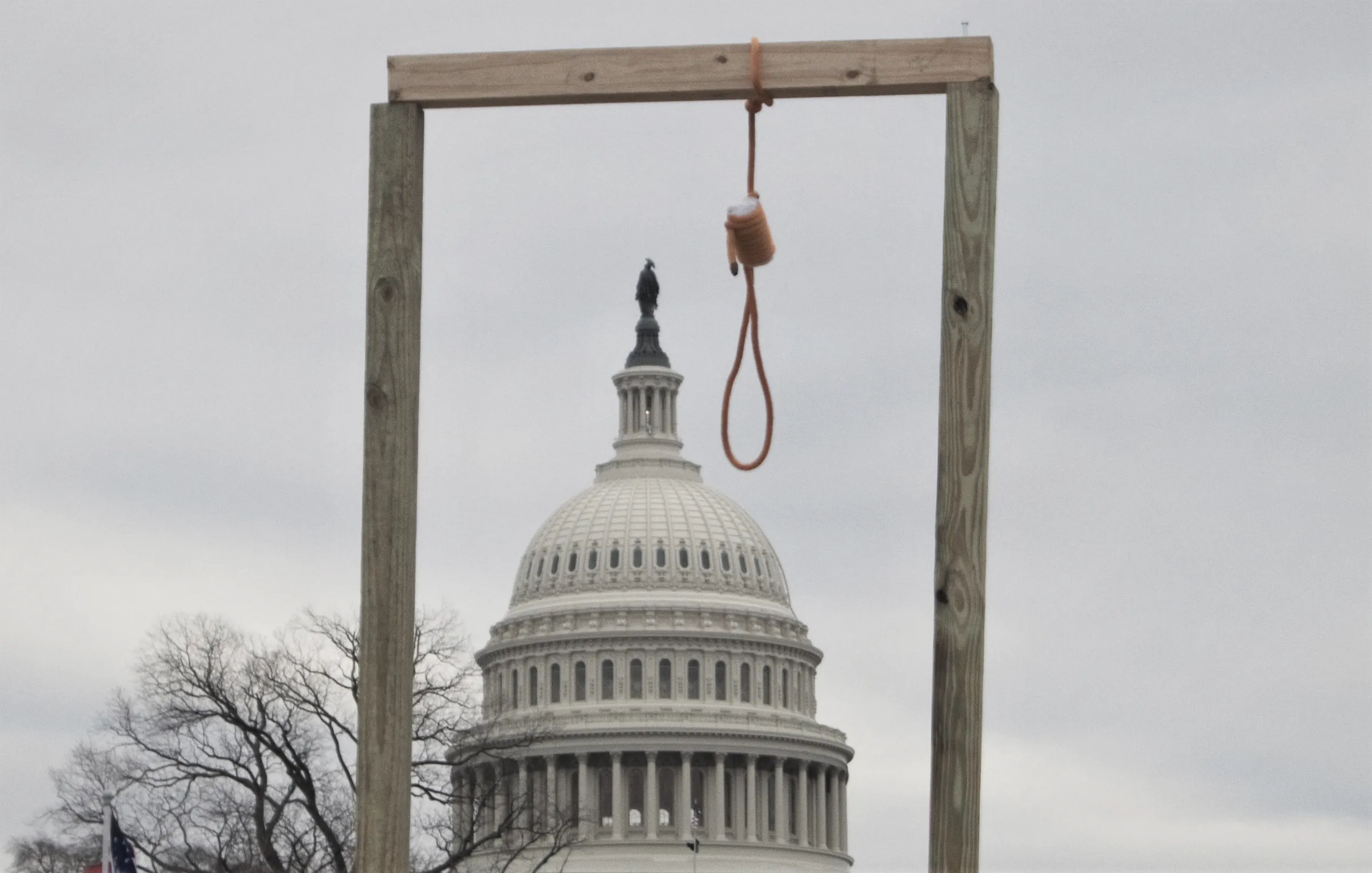 A wooden gallows with an orange noose, built by the crowd on 6 January 2021, with the dome of the US Capitol framed between its posts.