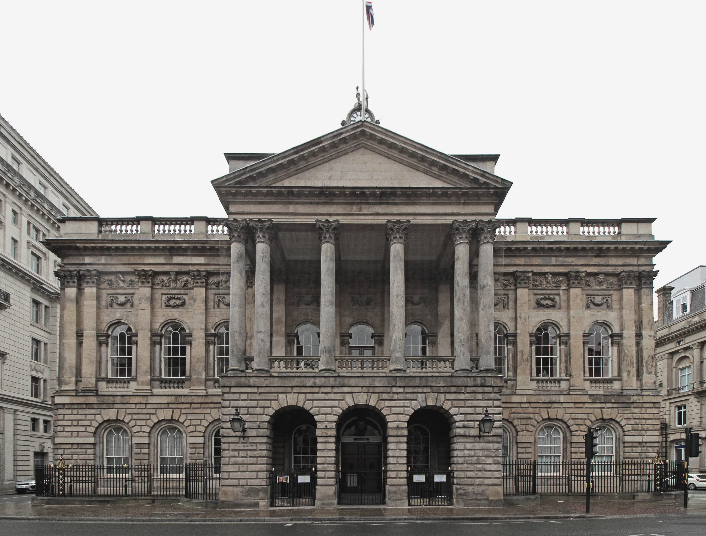 The front of Liverpool Town Hall: a stone portico with six columns above three arched entrances, seen from the street in grey light.