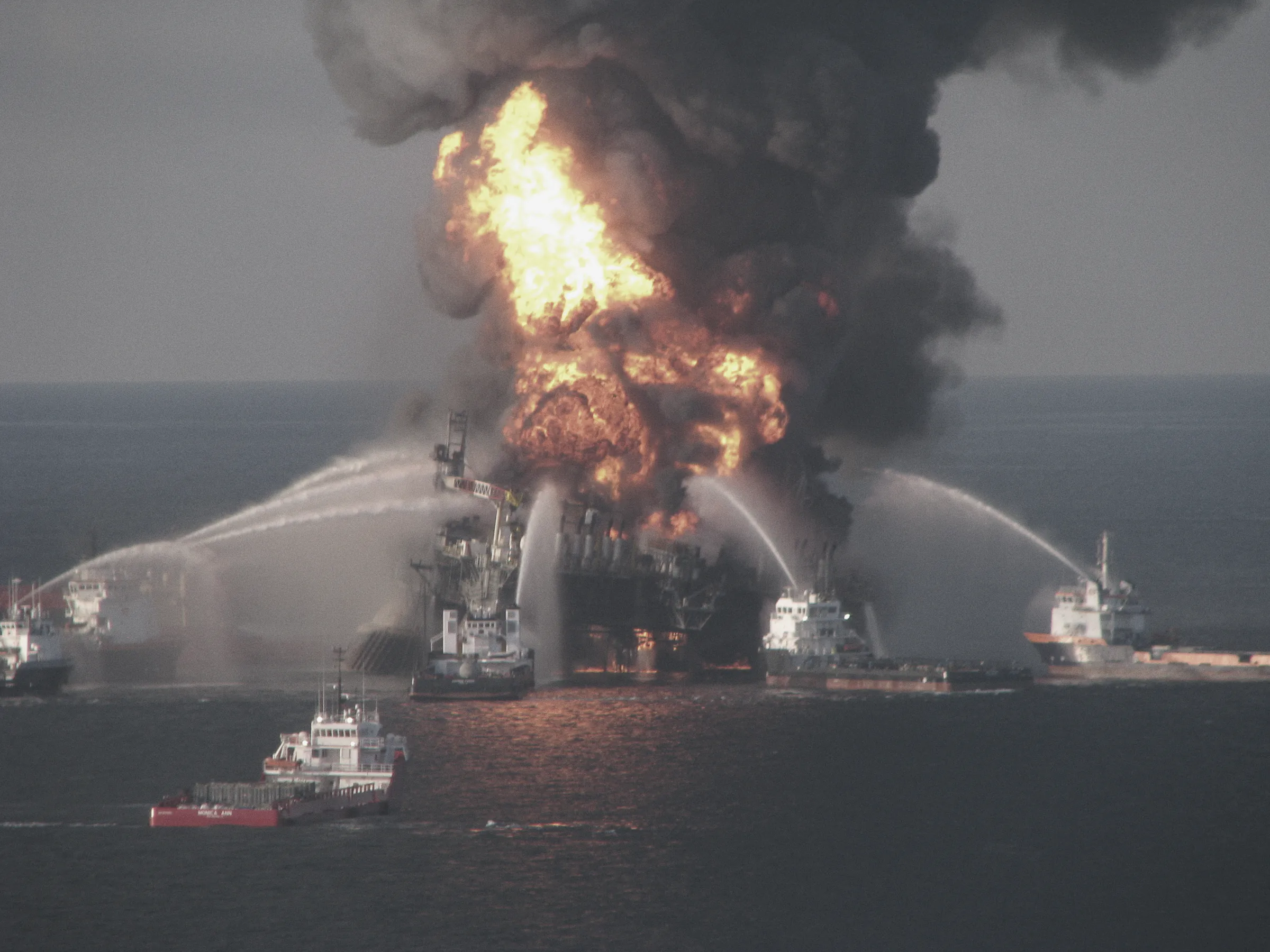Fire boats spray water on the Deepwater Horizon rig in the Gulf of Mexico on 21 April 2010, flames and black smoke pouring from it.